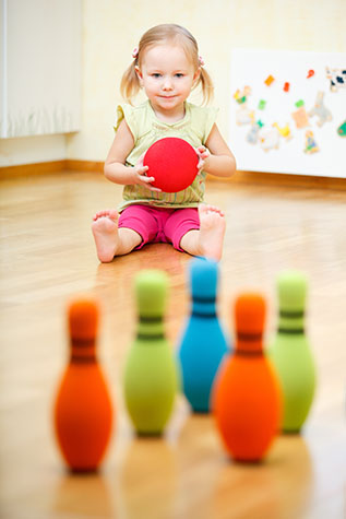 Adorable toddler girl playing bowling at home
