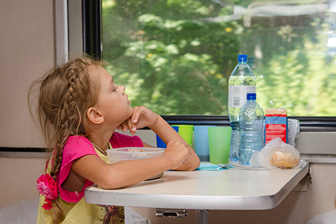 A six-year girl in a train sitting at a table with food on a lower place in the second-class compartment of the car and looks thoughtfully out the window