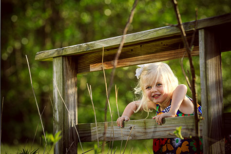 Blonde caucasian girl playing outside in cute dress by wooden bridge