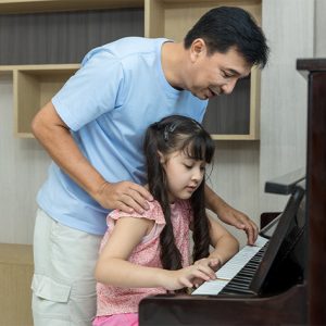 dad standing over a child who is playing piano